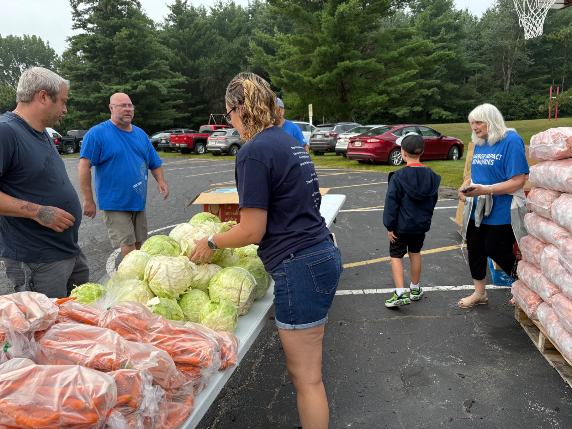 Volunteers organize a pile of cabbages and pallets of carrots at a drive-through giveaway.